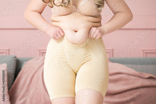 Fat woman in corrective panties, flabby belly and hips after pregnancy, overweight female body on pink background, body care concept © staras