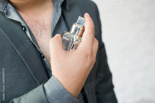 Handsome man applying perfume on neck against a light background, close up