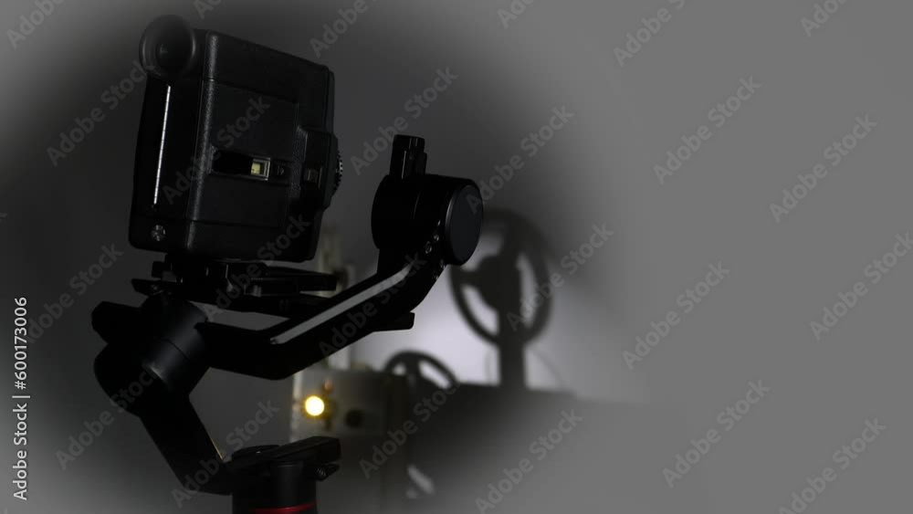 An old movie camera works on an automatic steadicam against the background of a movie projector. An old movie camera works on an automatic steadicam against the background of a movie projector.