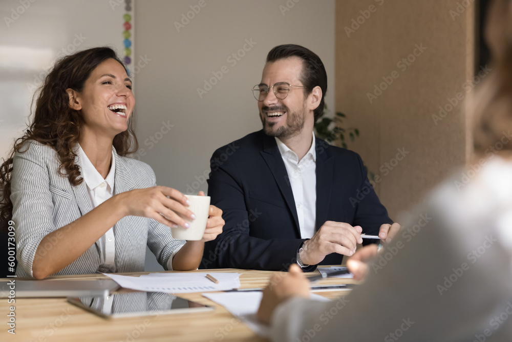 Laughing colleagues engaged in group briefing gathered in conference room, drink coffee enjoy communication distracted from business enjoy good work relations, joking feel happy take part in teamwork Laughing colleagues engaged in group briefing gathered in conference room, drink coffee enjoy communication distracted from business enjoy good work relations, joking feel happy take part in teamwork