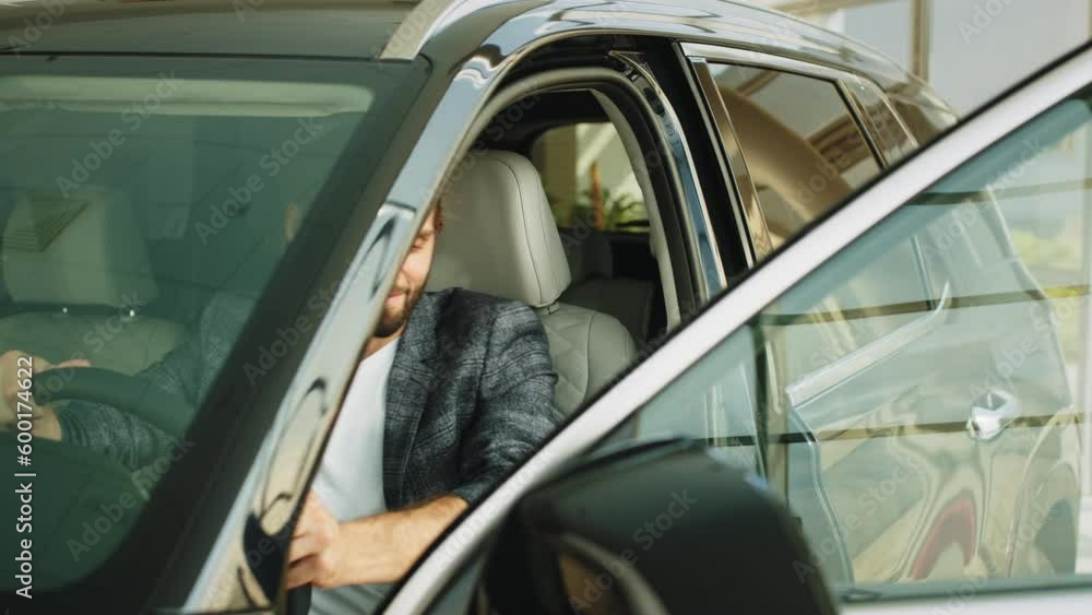 A elderly man with friendly Helpful car salesman in a car dealership are studying the interior of a new car through an open door. Two men elderly father and adult son in a showroom choose a new car A elderly man with friendly Helpful car salesman in a car dealership are studying the interior of a new car through an open door. Two men elderly father and adult son in a showroom choose a new car