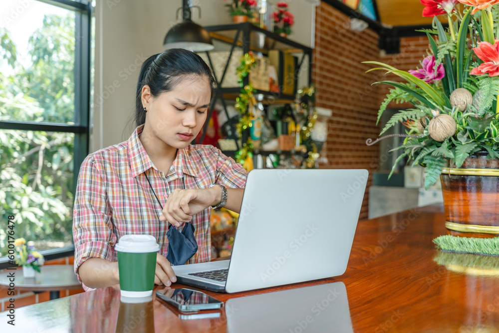 Fototapeta premium Asian businesswoman looking serious looking at wrist watch frustrated with a video call from a customer who is not on time or stressed with work, the unhappy woman checking time anxiety