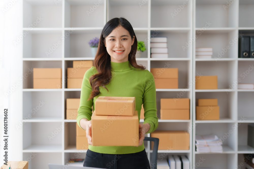 Smiling young Asian business owner woman prepare parcel box and check online orders of product for deliver to customer on laptop computer at home. Shopping Online concept. Startup small business SME. Smiling young Asian business owner woman prepare parcel box and check online orders of product for deliver to customer on laptop computer at home. Shopping Online concept. Startup small business SME.