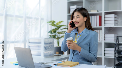 Happy beautiful smiling Asian businesswoman talking on mobile phone while working in office.