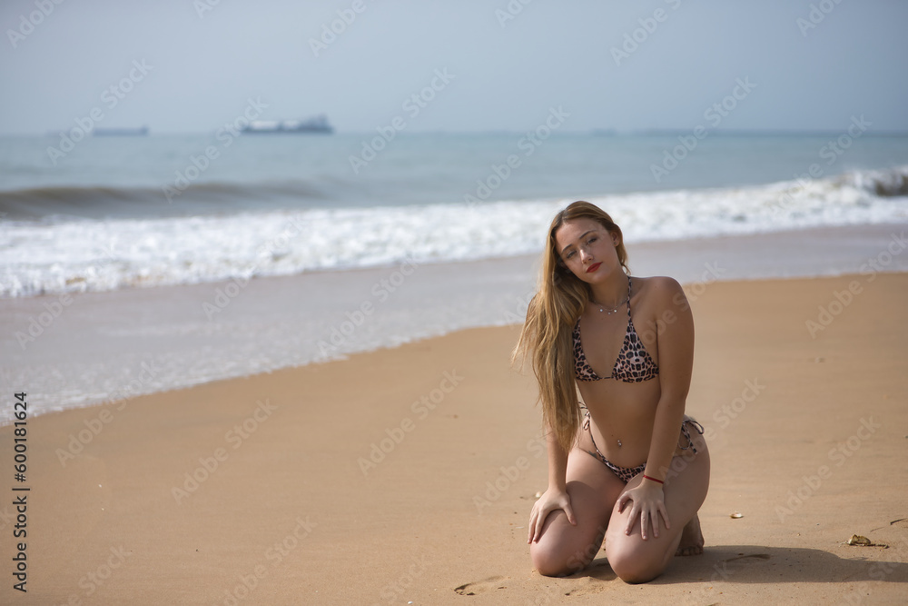 Young, blonde, beautiful woman, wearing a leopard print bikini, kneeling on the shore of the beach, relaxed, lonely and calm. Concept beach, bikini, relax, peace, tranquility. Young, blonde, beautiful woman, wearing a leopard print bikini, kneeling on the shore of the beach, relaxed, lonely and calm. Concept beach, bikini, relax, peace, tranquility.