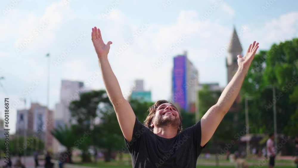 Faithful young man raises arms to sky feeling GRATEFUL standing outdoors in urban city. A male person celebrates LIFE with HOPE Faithful young man raises arms to sky feeling GRATEFUL standing outdoors in urban city. A male person celebrates LIFE with HOPE