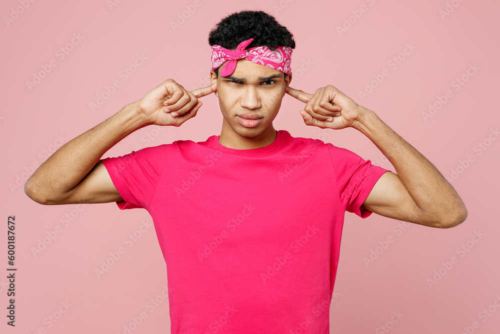Young sad man of African American ethnicity he wears headscarf t-shirt casual clothes cover ears with hands fingers do not want to listen scream isolated on pastel plain light pink color background. Young sad man of African American ethnicity he wears headscarf t-shirt casual clothes cover ears with hands fingers do not want to listen scream isolated on pastel plain light pink color background.