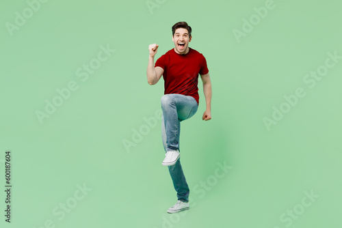 Full body young brunet man he wears red t-shirt casual clothes doing winner gesture celebrate clenching fists say yes isolated on plain pastel light green background studio portrait Lifestyle concept © ViDi Studio