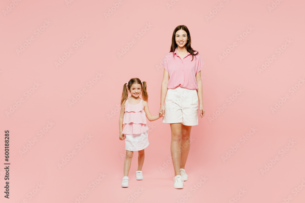 Full body smiling woman wear casual clothes with child kid girl 6-7 years old. Mother daughter look camera hold hands walk together isolated on plain pastel pink background. Family parent day concept. Full body smiling woman wear casual clothes with child kid girl 6-7 years old. Mother daughter look camera hold hands walk together isolated on plain pastel pink background. Family parent day concept.