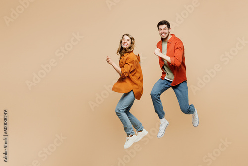 Full body side view young couple two friends family man woman wear casual clothes together jump high run fast hurry up looking camera isolated on pastel plain beige color background studio portrait.