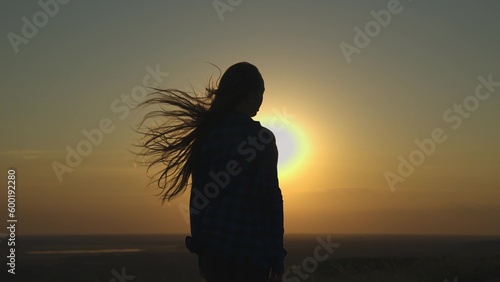 young girl looks at sunset and prays, religious person, her hair is flying in wind in glare of the sun, to believe in goodness, a woman\'s dream of love, to think and ask for forgiveness from heaven