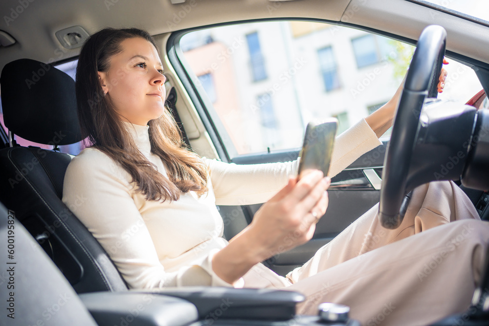 Young woman sitting in car and using smart phone, business woman busy driving