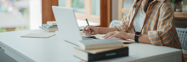 Young woman student busy study make notes in notebook and using laptop concentrated online training course technology education.