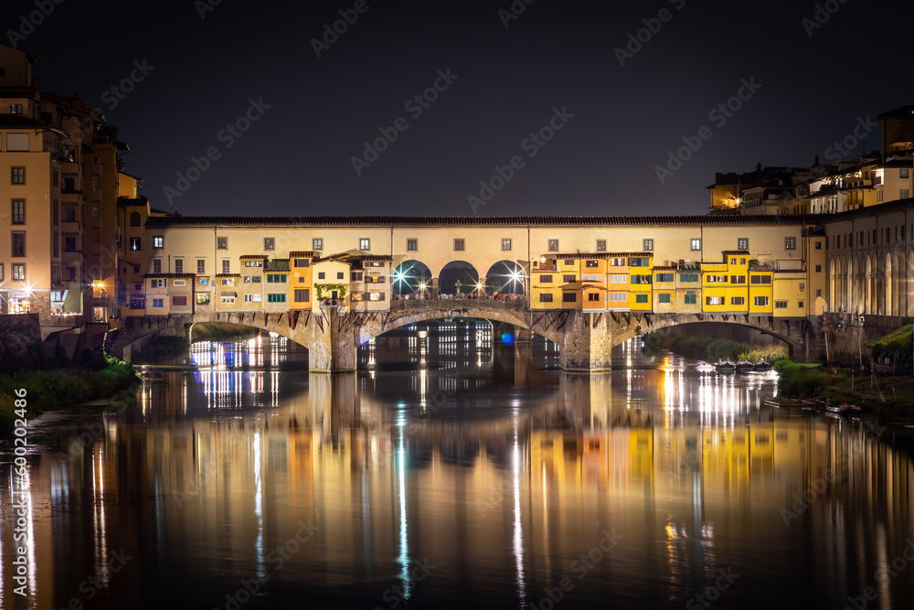 Ponte Vecchio at night. Reflections of colorful city lights in the river. Florence, Italy.