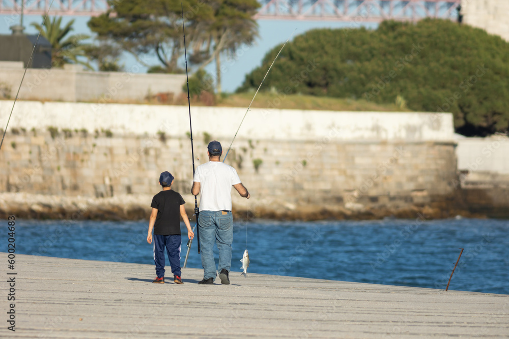 Father and son walking along the pier holding fish hanging on a fishing line Father and son walking along the pier holding fish hanging on a fishing line