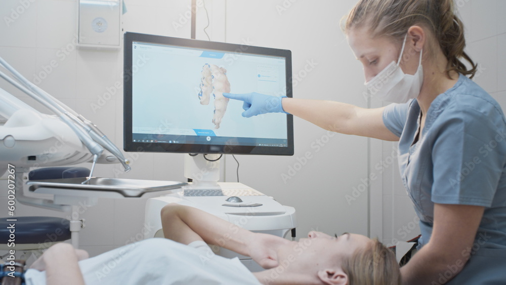 Obraz premium Girl doctor dentist demonstrates a 3D model of teeth on a touch monitor. Dental consultation in the clinic, diagnostics