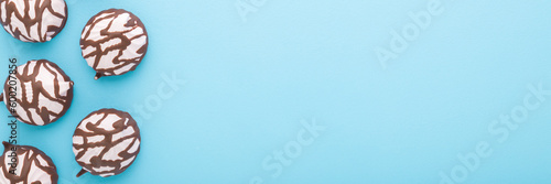 Pink soft zephyr covered with dark brown chocolate glaze on light blue table background. Pastel color. Closeup. Sweet snack. Food wide banner. Empty place for text. Top down view.