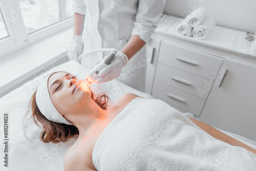 Canvas Print The beautician conducts light therapy of the face in a beauty clinic using an LED device