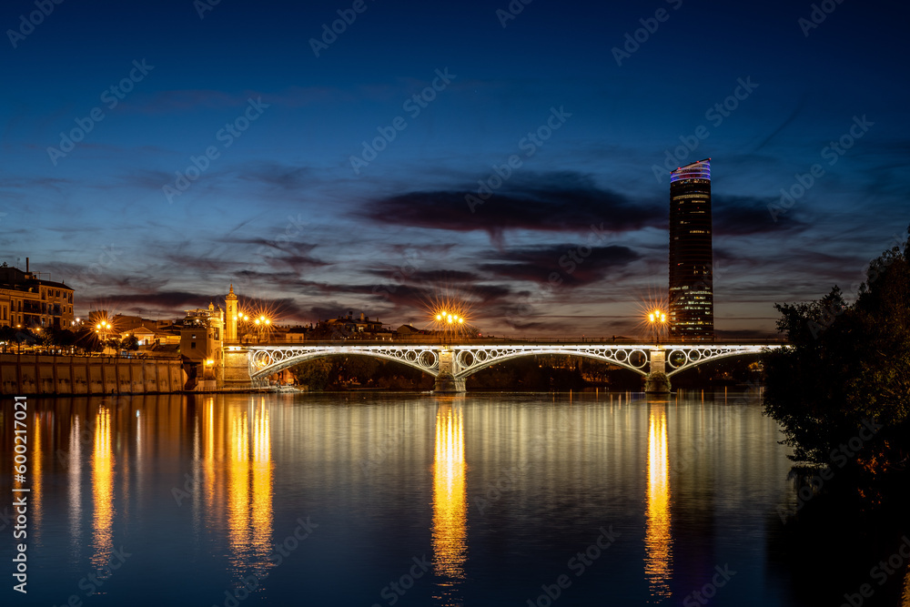 Torre Sevilla and Puente de Isabel II reflected in the river Guadalquivor during blue hour. Sevilla, Spain.