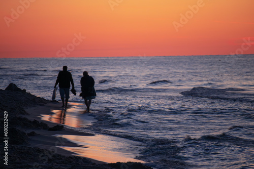 Para seniorów spacerująca brzegiem plaży o zachodzie słońca