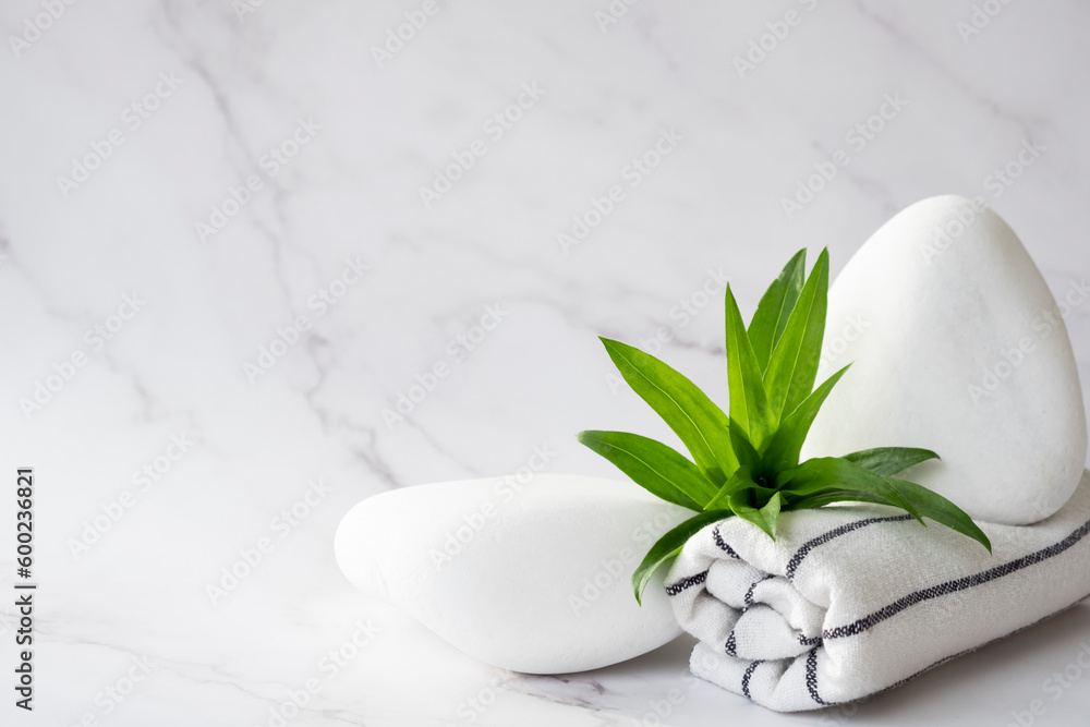 SPA background concept. White stones, towel, and leaves of green plant on marble background with copy space. Body care and beauty treatment. Spa and wellness or beauty salon concept. Copy space. SPA background concept. White stones, towel, and leaves of green plant on marble background with copy space. Body care and beauty treatment. Spa and wellness or beauty salon concept. Copy space.