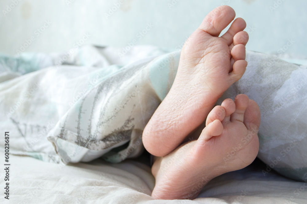 Feet under a light blanket on the bed. Concept of sleeping or waking in the morning Feet under a light blanket on the bed. Concept of sleeping or waking in the morning