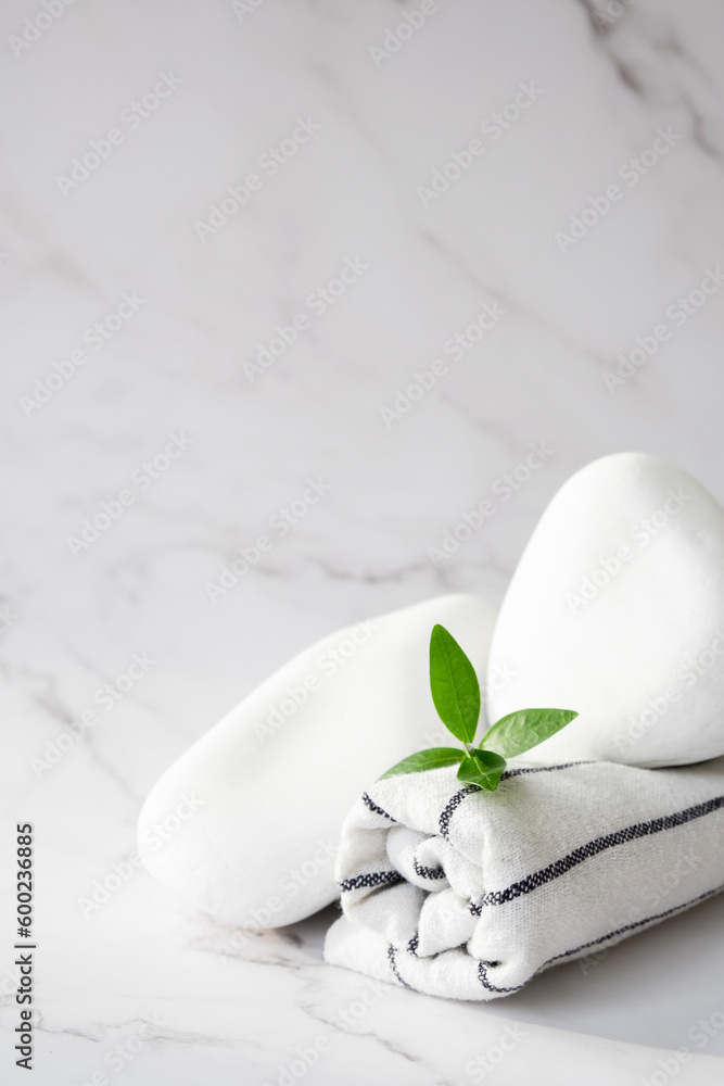 SPA background concept. White stones, towel, and leaves of green plant on marble background with copy space. Relaxation, body care and beauty treatment concept.