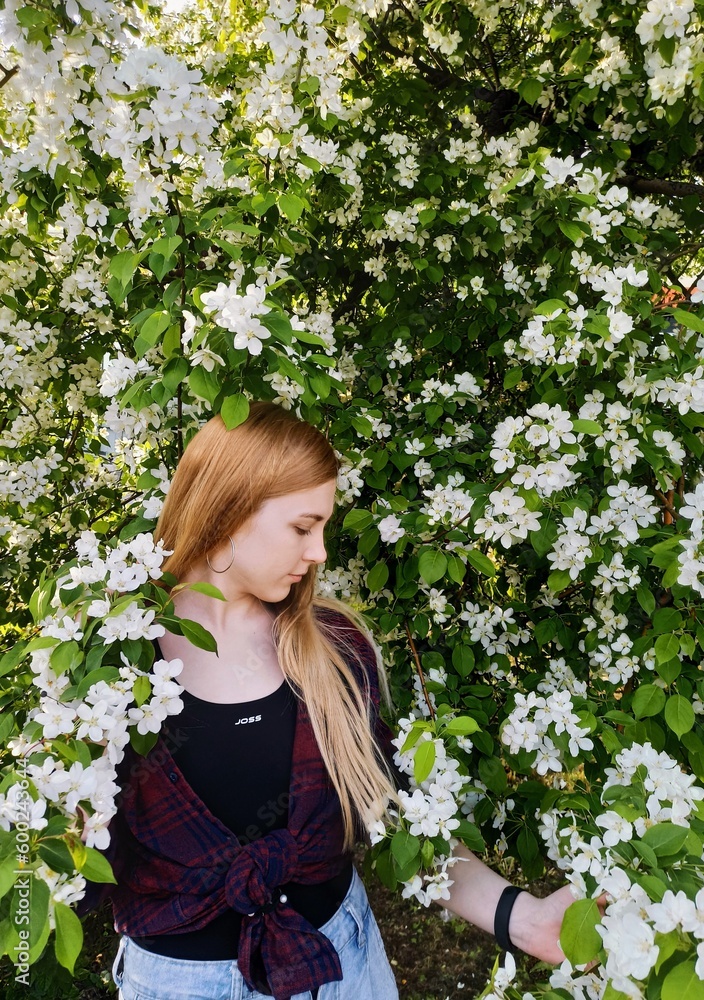 A young girl in a checkered shirt against the background of a blooming apple tree. A young girl in a checkered shirt against the background of a blooming apple tree.