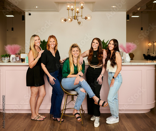 CONROE, TEXAS, USA - APRIL 14th 2023: 5 female managers of a beauty salon are posing for a business portrait in the salon against their company logo. Thel have professional makeup and hair extensions photo