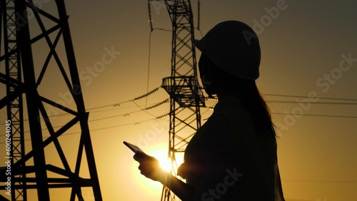 silhouette of an electrical engineer. engineer work tablet sunset. studying electrical technology near industry. towers electricity work. tower electricity power engineer tablet. digital working