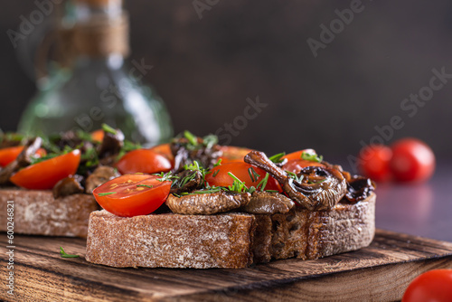 Close-up of bruschetta on rye bread with cherry tomatoes and fried mushrooms on a wooden board