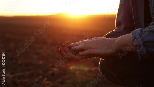 Male farmer's hand holds a handful of dry ground and checks soil fertility and quality before sowing crops on plowed field at sunset. Cultivated land. Concept of organic agriculture and agribusiness.