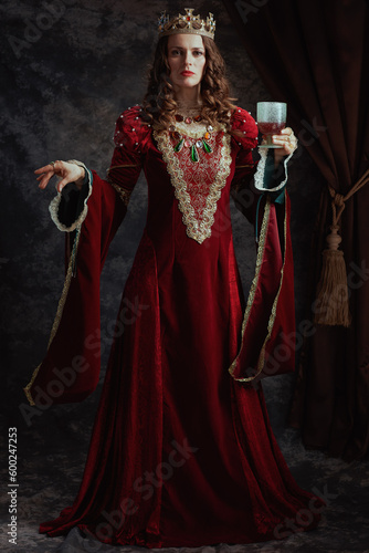 Full length portrait of medieval queen in red dress with goblet