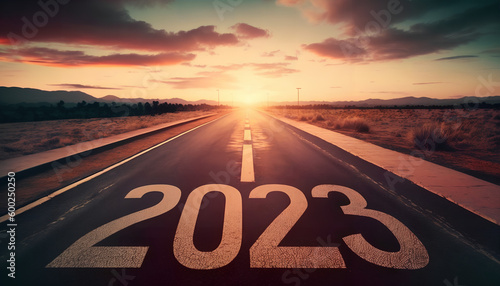 New year 2023 or start straight concept.word 2023 written on the asphalt road and athlete woman runner stretching leg preparing for new year at sunset.Concept of challenge or career path and change