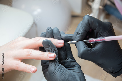 the manicurist levels the edge of the varnish with a thin brush in a salon