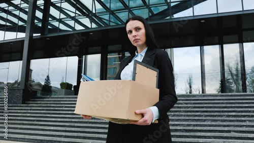 A person sits outside, holding a cardboard box with a worried expression after experiencing job loss and workloss. photo