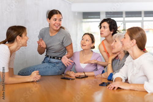 Women of different ages in casual clothes communicate at table in office..