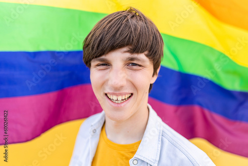 Young gay man smiling at camera over rainbow flag background. LGBT people concept