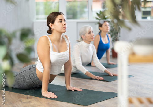 Sport women who take care of their physical health and do yoga in group workouts, practice the cobra pose in the gym