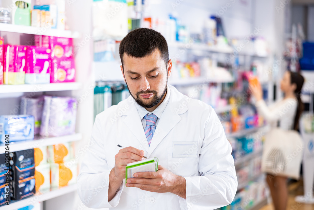 Young adult man pharmacist holding notepad and pen working at pharmacy