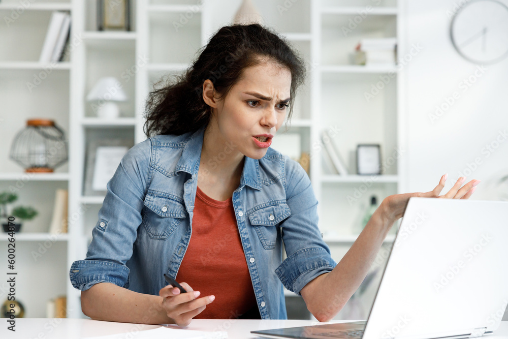 Disappointed girl looks at the laptop screen, does not understand what happened. Brunette woman is angry that the computer broke. Disappointed girl looks at the laptop screen, does not understand what happened. Brunette woman is angry that the computer broke.