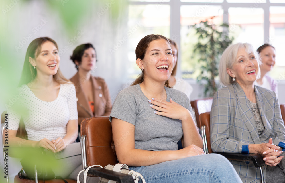 Young smiling woman in casual clothes listening to speaker lecture while sitting in office