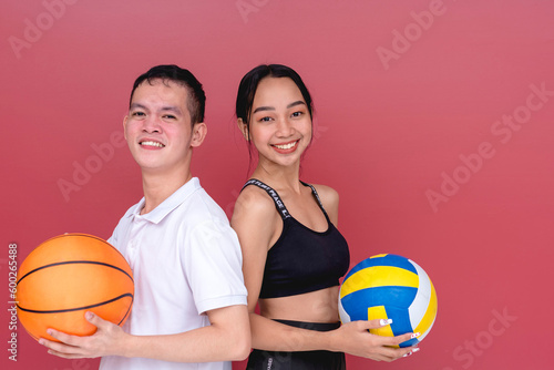 Photos Two young and active players posing back to back while holding a volleyball and a basketball