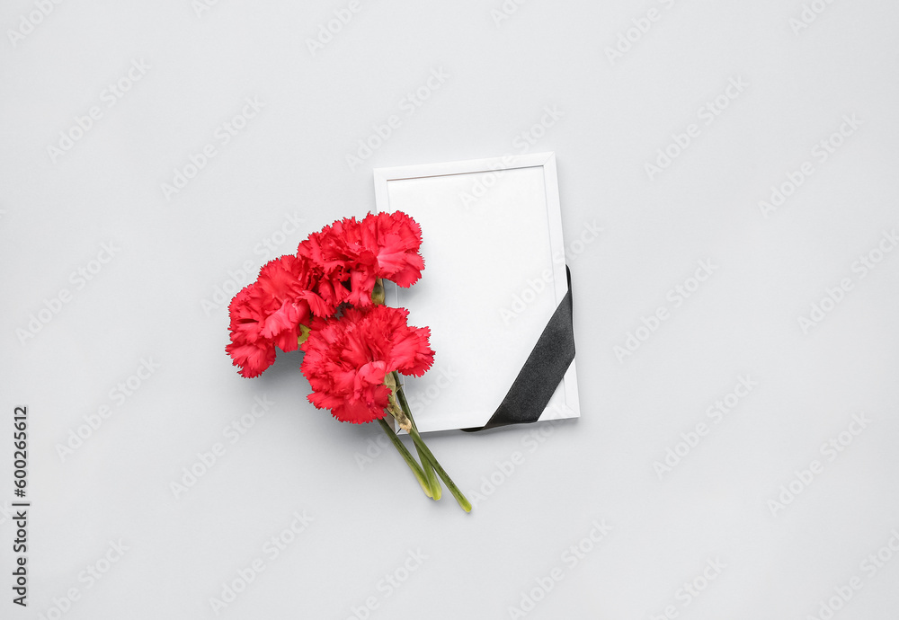 Red carnations with black ribbon and photo frame on light background Red carnations with black ribbon and photo frame on light background