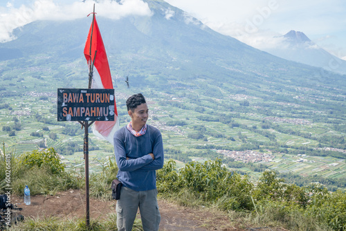 Young man Indonesian reach peak of mountain. The photo is suitable to use for adventure content media, nature poster and forest background.