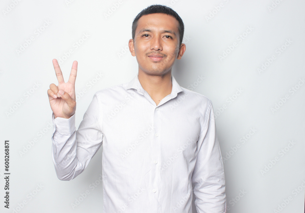 Smiling young Asian man wearing white shirt with hand peace sign isolated on white background. Smiling young Asian man wearing white shirt with hand peace sign isolated on white background.