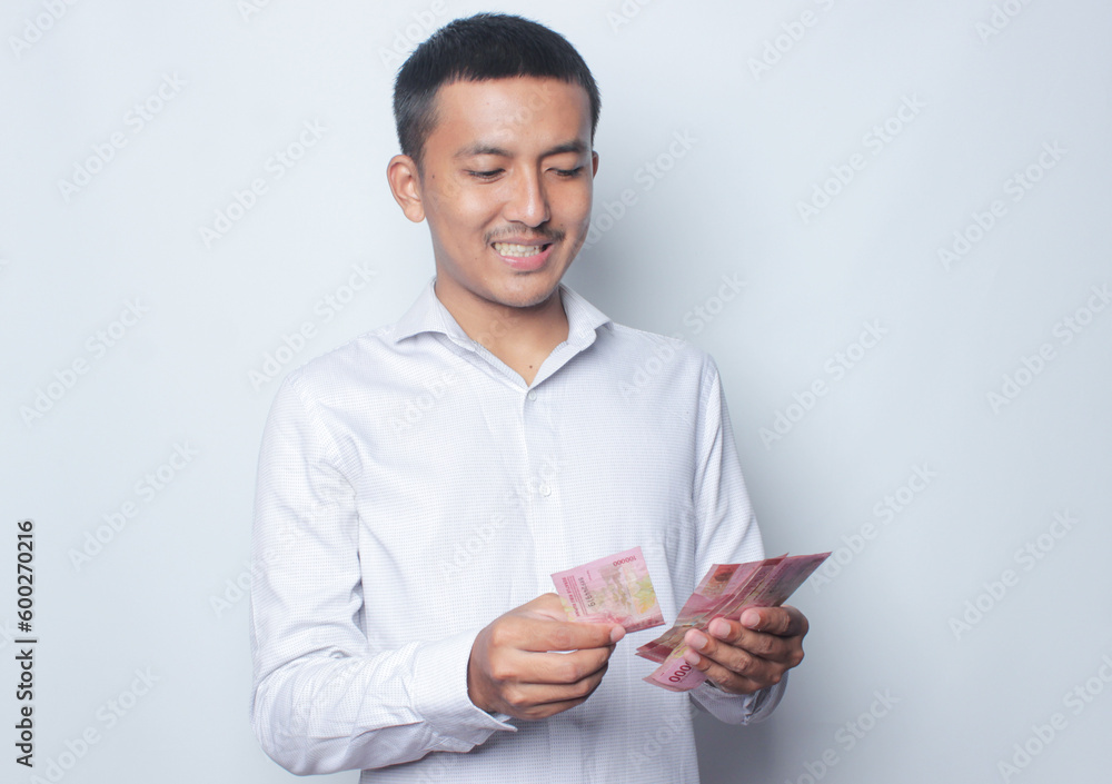 Asian young man holding paper money and showing happy expression. Isolated on white background. Asian young man holding paper money and showing happy expression. Isolated on white background.