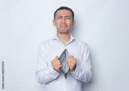 Asian young man looking camera with sad expression while open his wallet. Isolated on white background