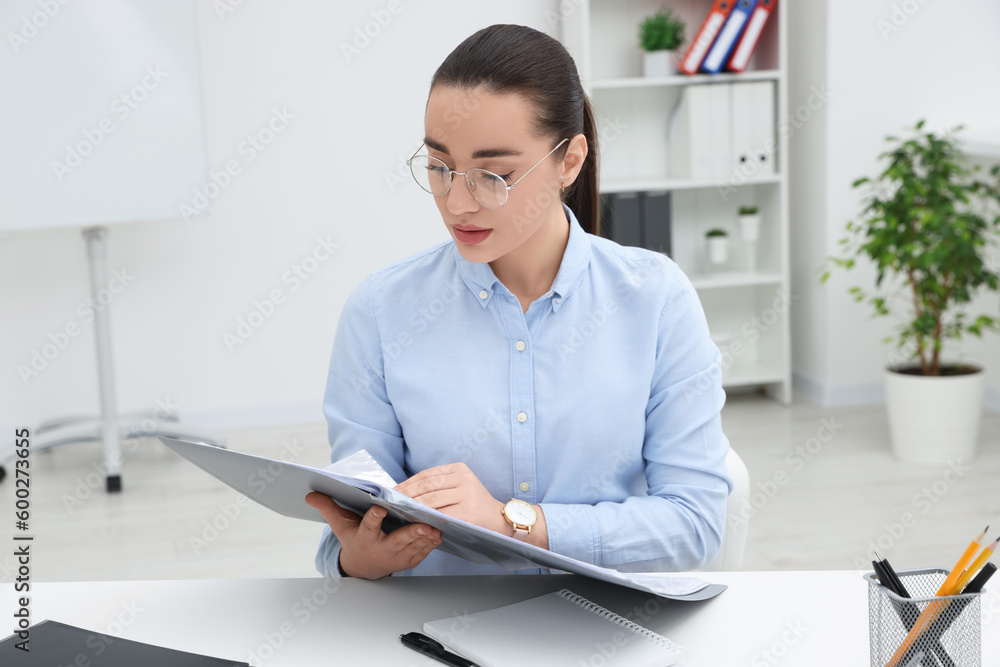 Young female intern with folder working at table in office Young female intern with folder working at table in office