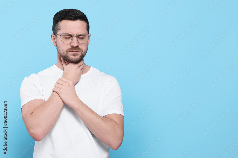 Man suffering from sore throat on light blue background, space for text Man suffering from sore throat on light blue background, space for text